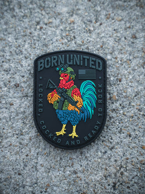 The Battle Bird PVC Patch by Born United Private Label features a colorful rooster in military gear with a rifle, “BORN UNITED” at the top, and “LOCKED, COCKED AND READY TO ROCK” at the bottom, set against a rough concrete surface.