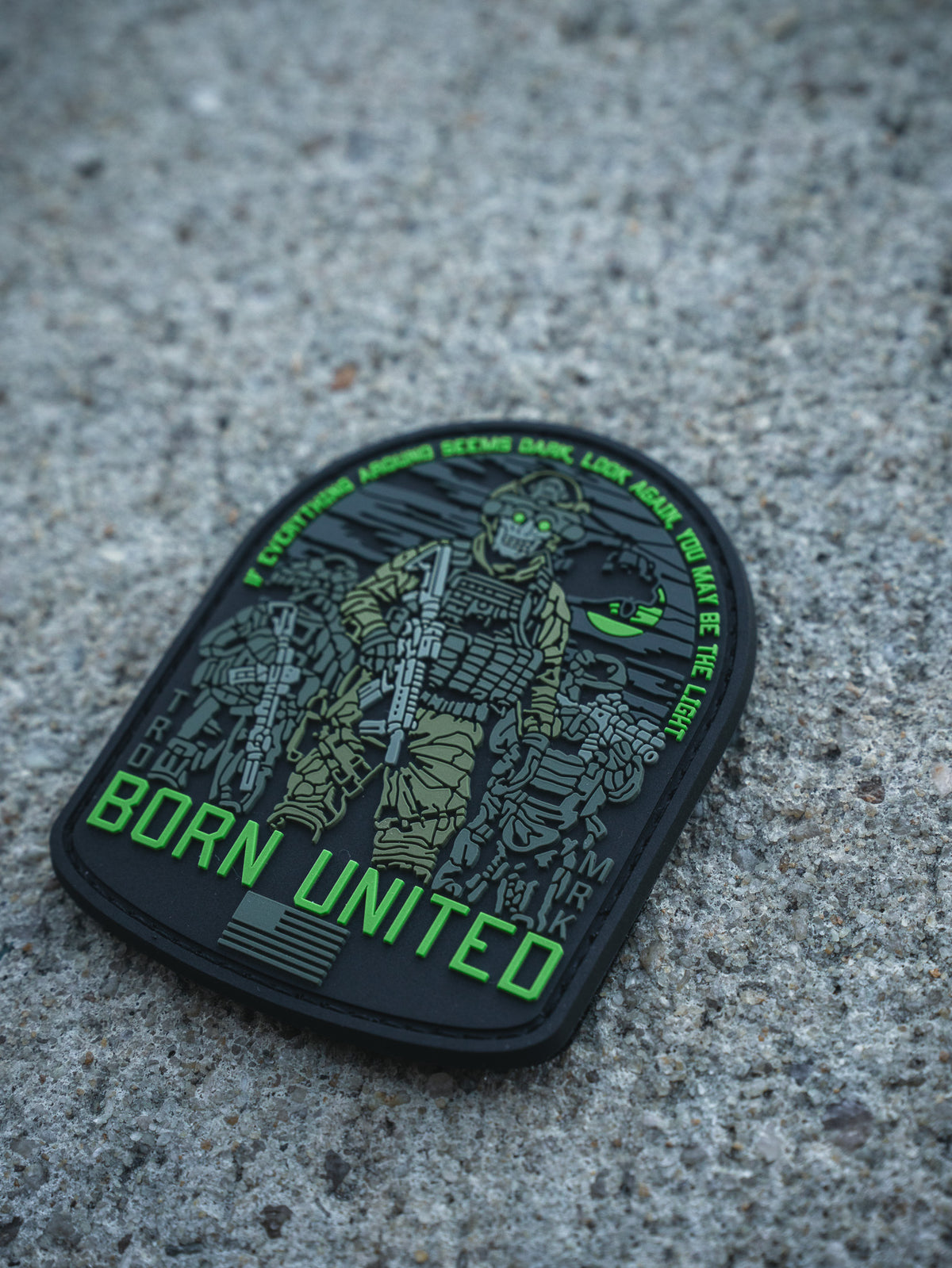 The Light in the Darkness PVC Patch by Born United Private Label features an armed soldier in night vision gear on concrete, "Born United" in bold green, and the quote: “Even if the world seems dark, look for the light. We are the light.”.