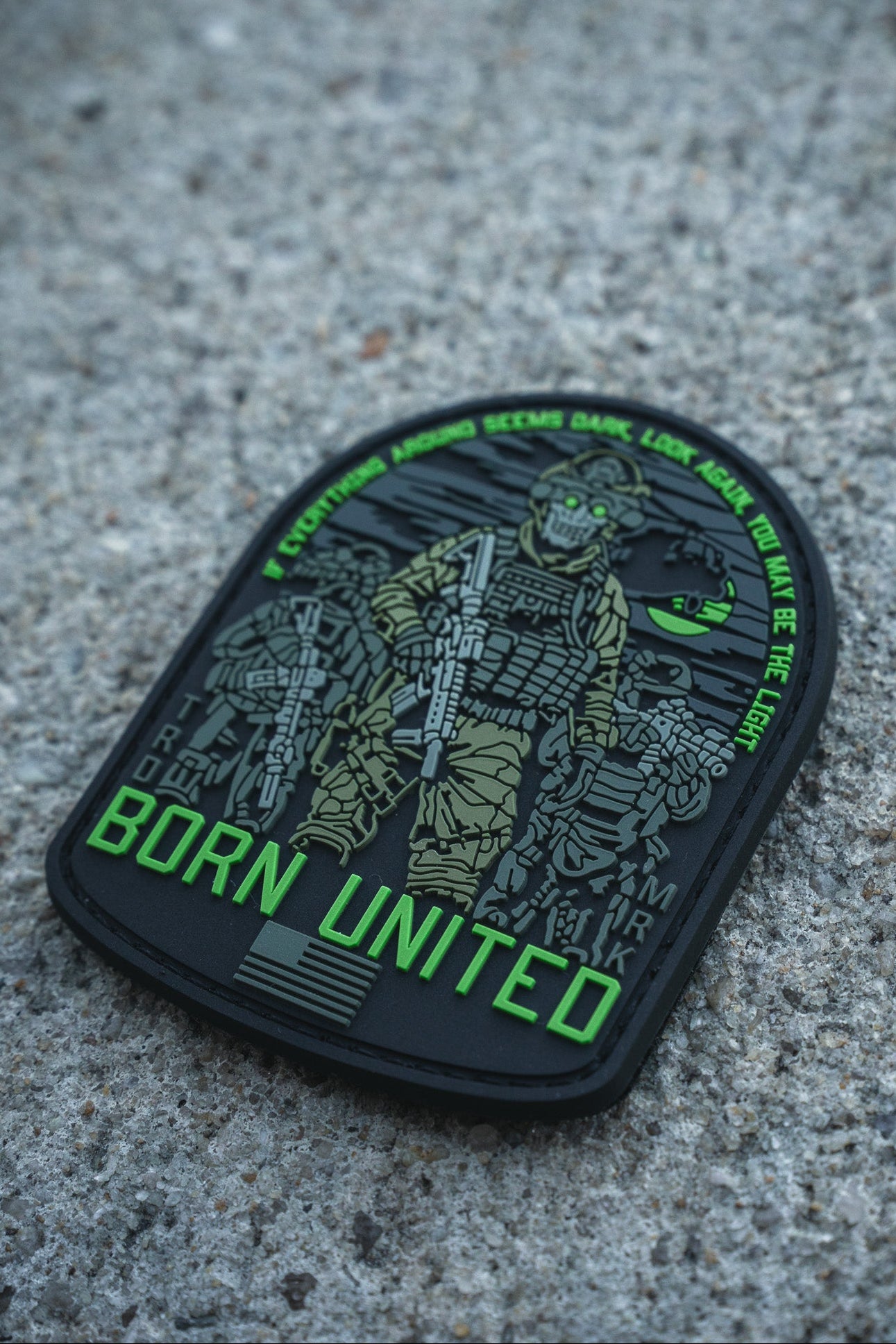 The Light in the Darkness PVC Patch by Born United Private Label features an armed soldier in night vision gear on concrete, "Born United" in bold green, and the quote: “Even if the world seems dark, look for the light. We are the light.”.