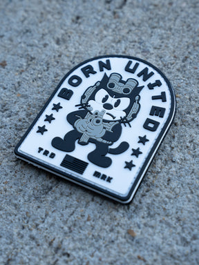 The Foxtrot Felix PVC Patch by Born United Private Label shows a cartoon cat in military gear holding a gun, set on black and white concrete with stars and "Born United" at the top, plus "TRD" and "MRK" at the bottom.