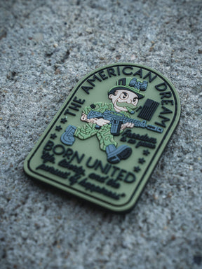 The American Dream PVC Patch by Born United Private Label features a cartoon soldier with a rifle on rough concrete, reading "THE AMERICAN DREAM," "Freedom Isn’t Free," and "BORN UNITED by unity we are powerfully unbreakable.