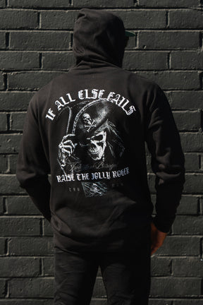 Wearing a Raise the Jolly Roger Hoodie by Relentless Betrayal, someone with pirate streetwear style stands before a black brick wall.