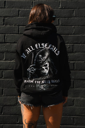 A person faces away in the Raise the Jolly Roger Hoodie by Relentless Betrayal, featuring a Grim Reaper and pirate streetwear text before a black brick wall.