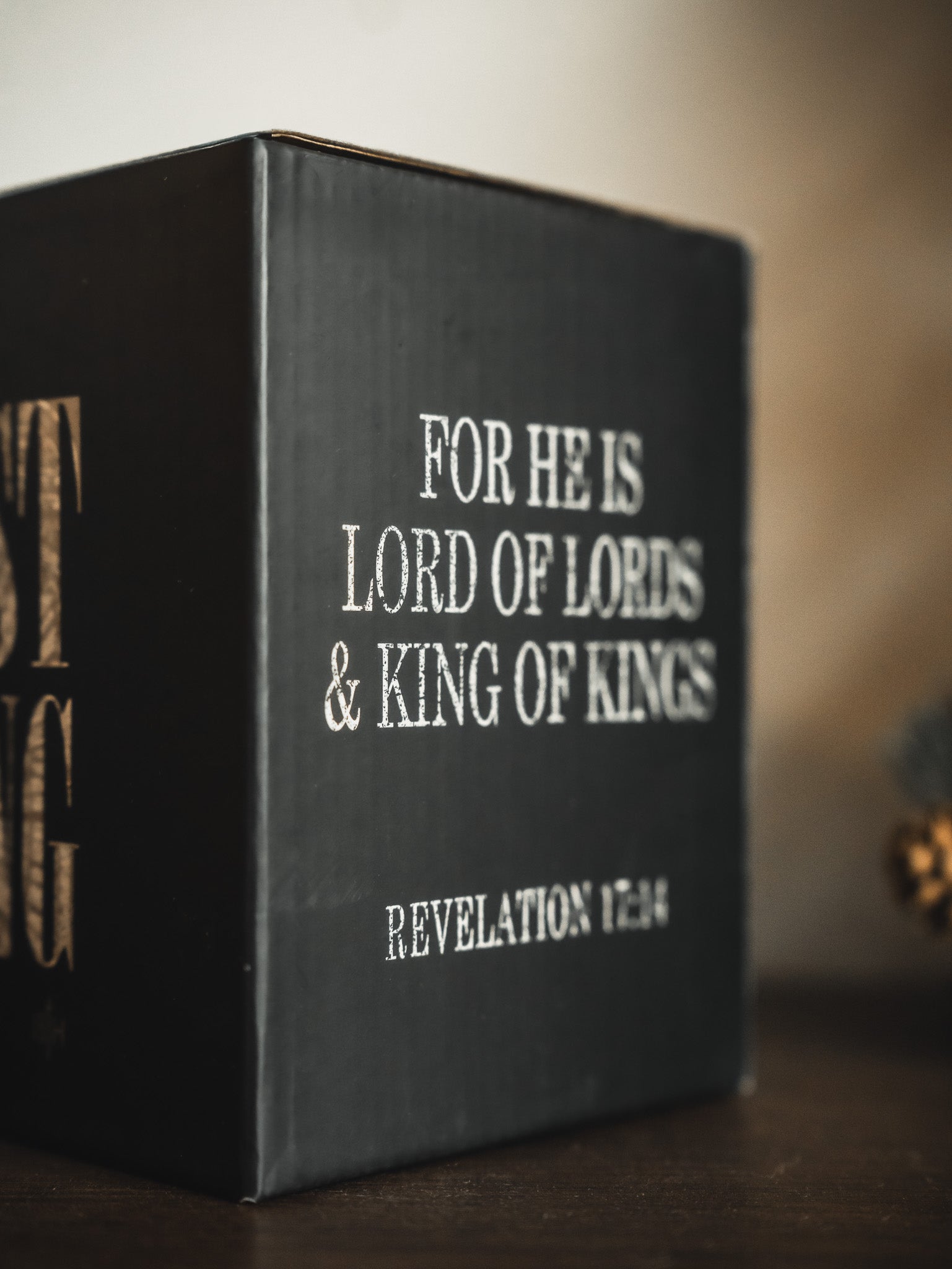 The Christ is King Mug by 13th features a black design with white text—FOR HE IS LORD OF LORDS & KING OF KINGS REVELATION 17:14—displayed on a wooden surface, serving as a daily reminder of Christ’s kingship.