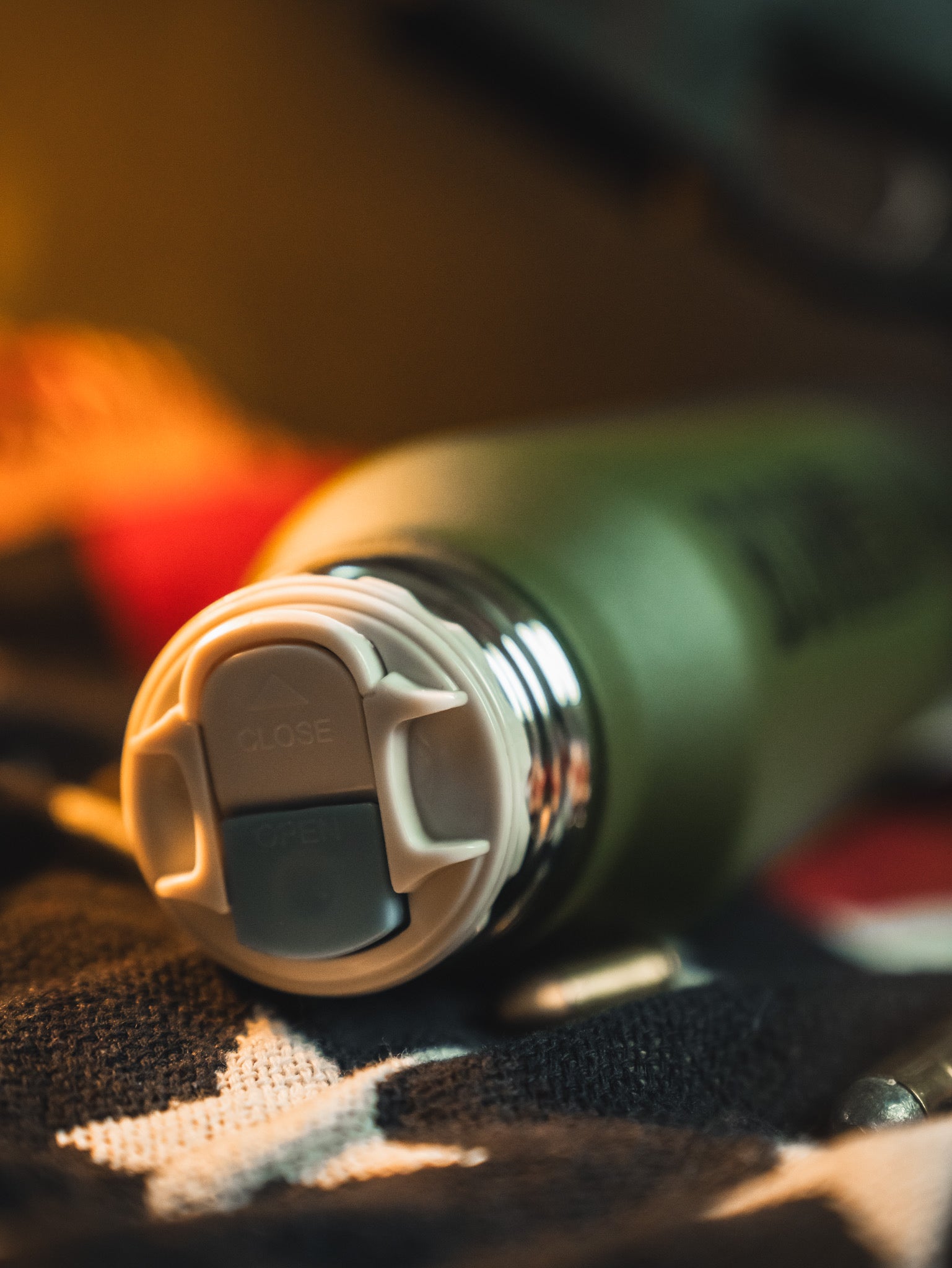 A close-up of the Born United Private Label Bullet Thermos, green with a gray cap featuring open/close markings, lies on a star-patterned fabric with a softly blurred background.