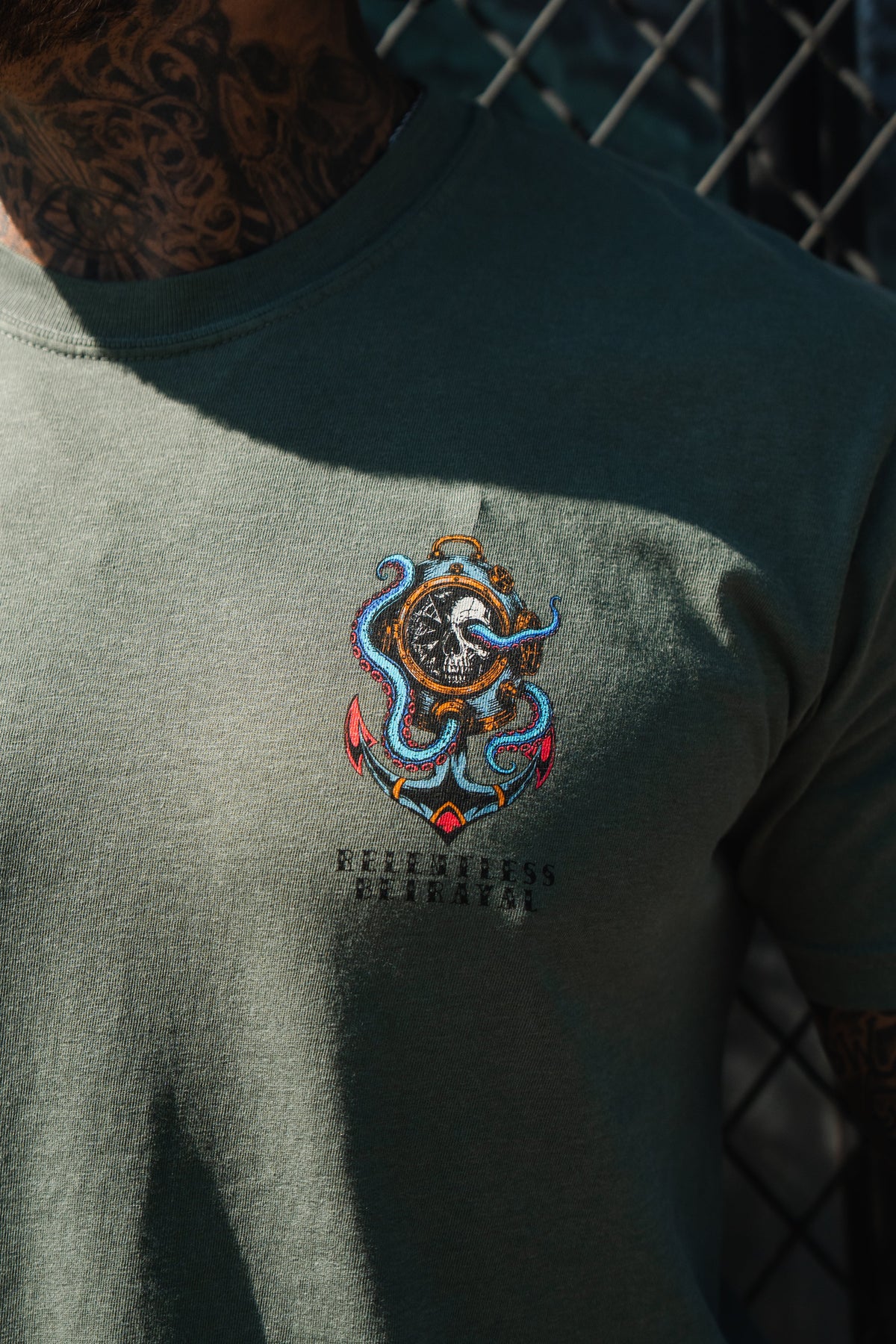 Wearing the Relentless Betrayal No Safe Harbor Premium T-Shirt - Olive, featuring a vivid octopus and helmeted figure graphic with partial text beneath.