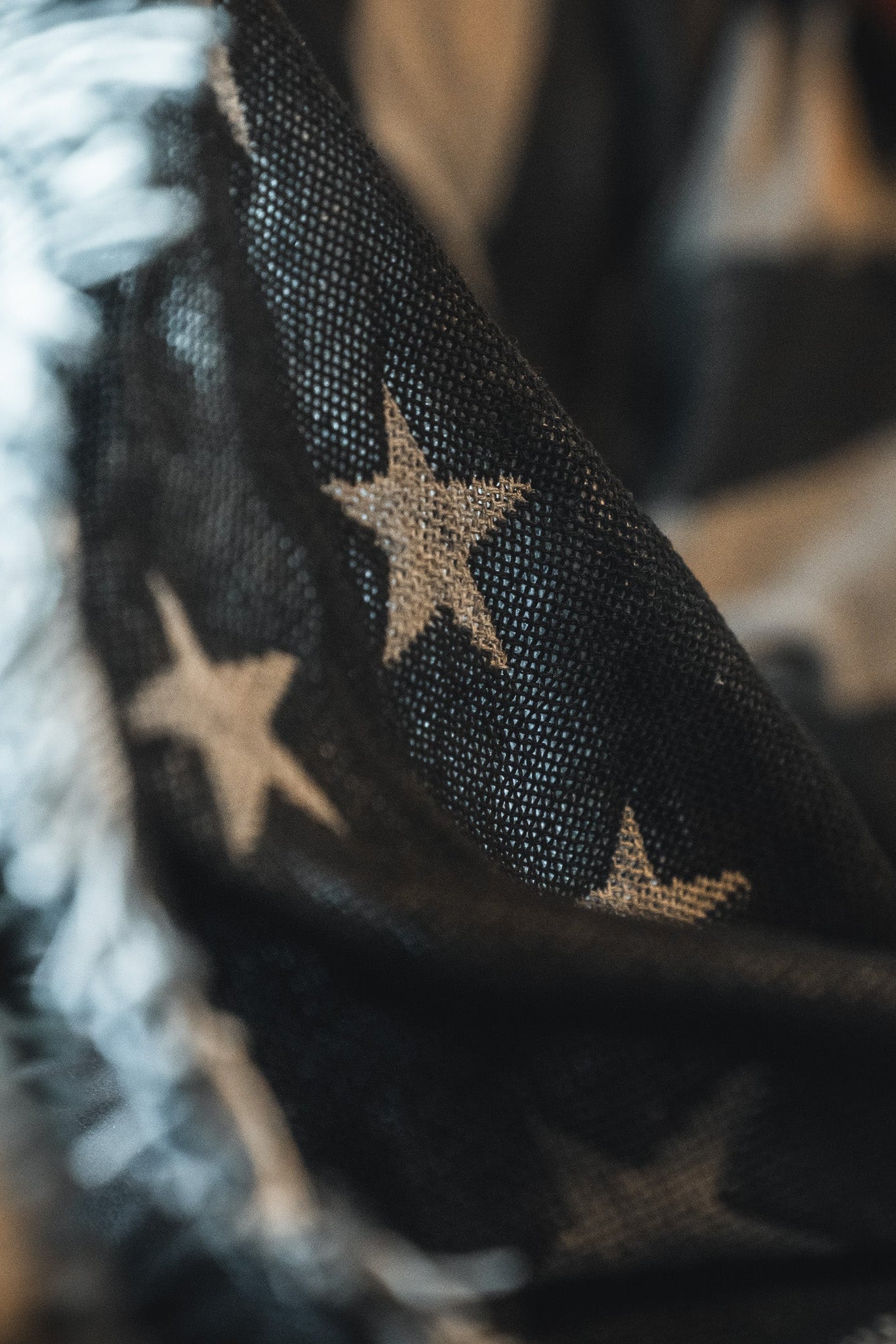 Close-up of the Born United Private Label Blackout American Flag Jacquard Blanket, showcasing its textured jacquard weave, white stars on a dark background, and frayed edges that evoke a classic patriotic feel.