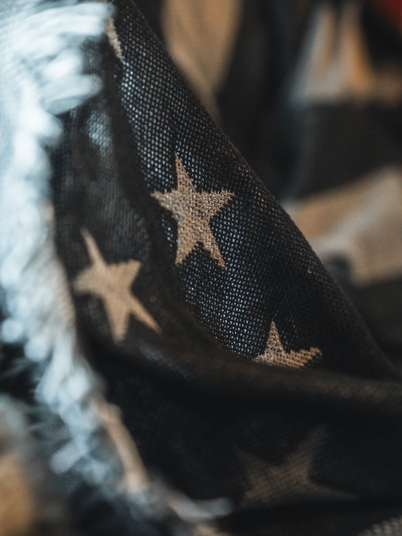 Close-up of the Born United Private Label Blackout American Flag Jacquard Blanket, showcasing its textured jacquard weave, white stars on a dark background, and frayed edges that evoke a classic patriotic feel.