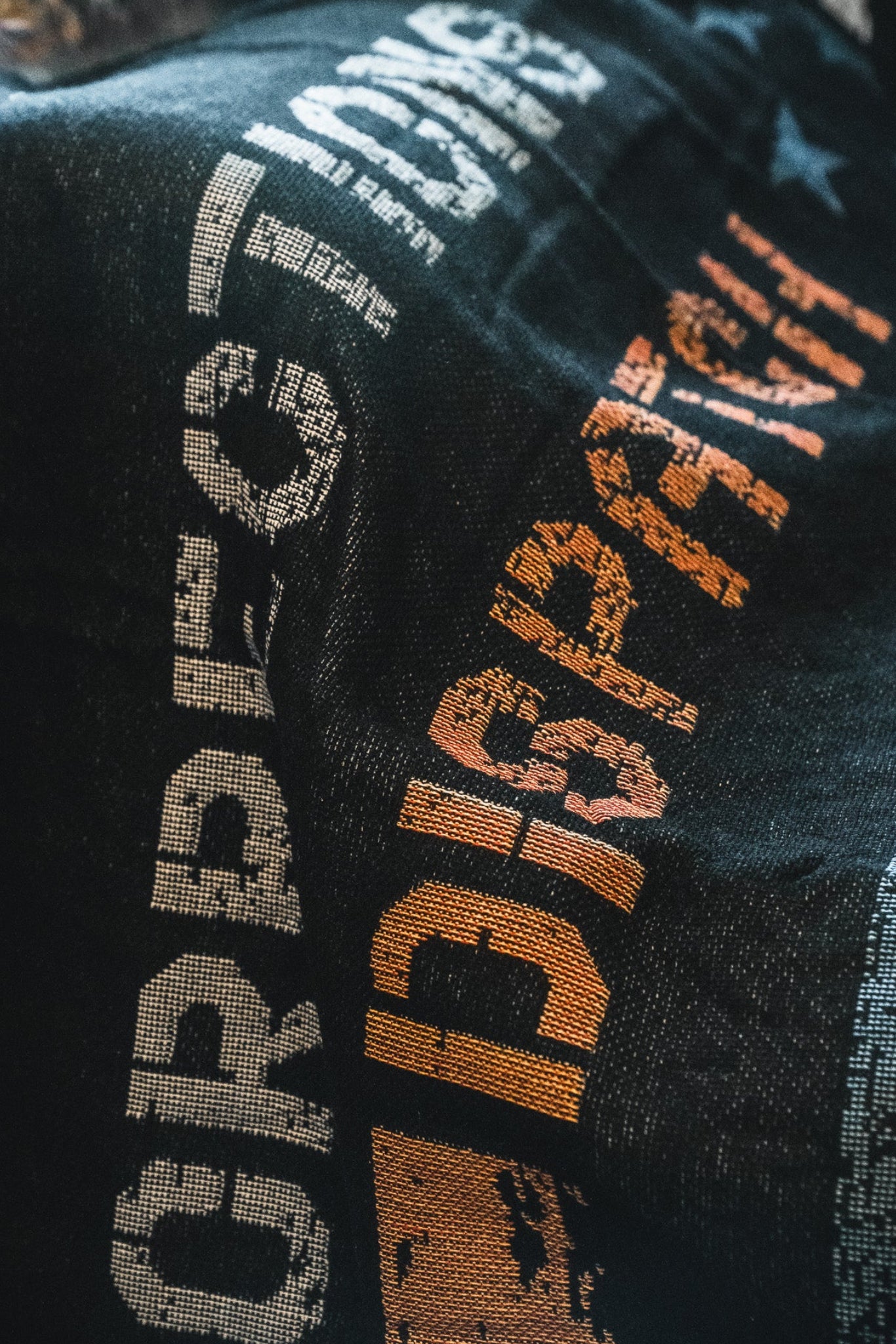 A close-up of the American Heroes Jacquard Blanket by Born United Private Label shows a dark woven design with “CORRECTIONS” in white and “DISPATCH” in orange, both partially visible and slightly textured.