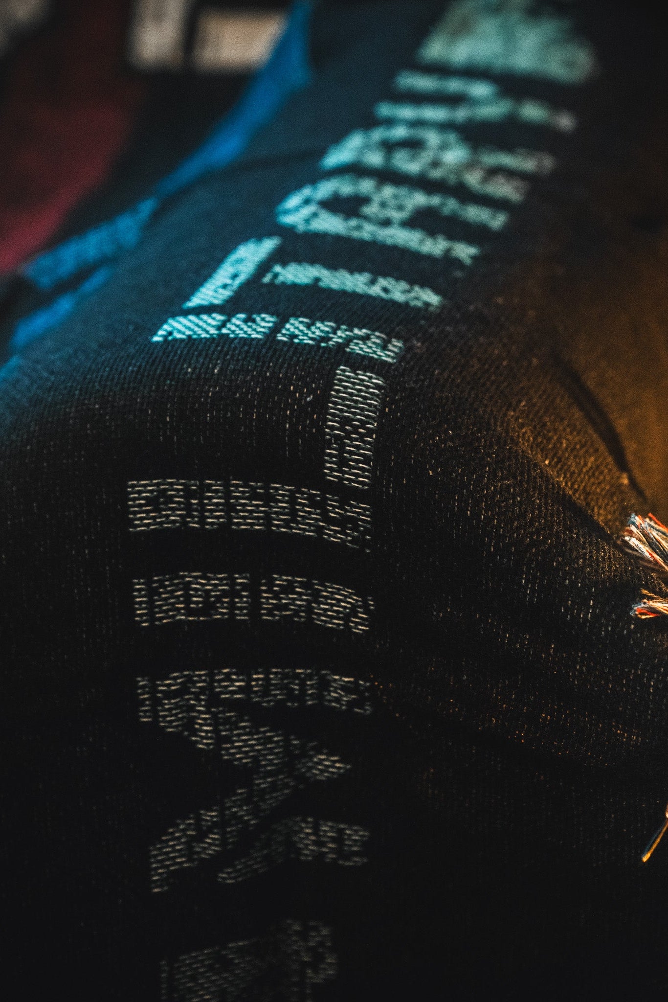 Close-up of dark denim fabric with light blue digital-style stitches and a decorative braided detail in orange, silver, and beige—echoing the design of the American Heroes Jacquard Blanket by Born United Private Label.