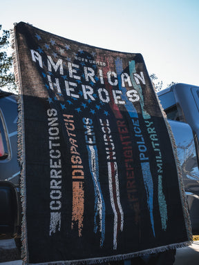 The Born United Private Label American Heroes Jacquard Blanket displays “American Heroes” with colorful faded stripes labeled Corrections, Dispatch, EMS, Firefighter, Police, and Military—perfect for draping over a vehicle.
