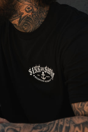 A tattooed individual wears a black Relentless Betrayal Dark Waters SOS T-Shirt, a unisex top with a white anchor and the words “Sink or Swim 2019 Relentless Brethren.”.