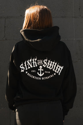 A person with straight, light brown hair faces away wearing the Relentless Betrayal Dark Waters SOS unisex hoodie. The black cotton-polyester hoodie’s back features “SINK OR SWIM, EST. 2019, RELENTLESS BETRAYAL” and an anchor graphic.