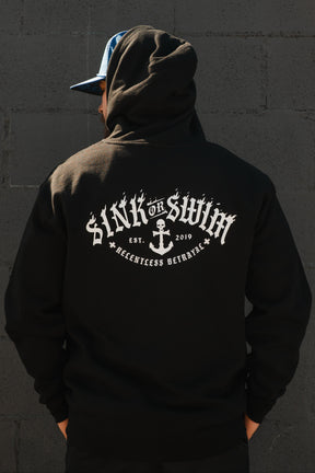 Wearing the Relentless Betrayal Dark Waters SOS Hoodie—a unisex cotton-poly blend with "SINK OR SWIM," skull and anchor graphic, "EST. 2019," and "RELENTLESS BETRAYAL" on the back—a person stands against a dark wall.