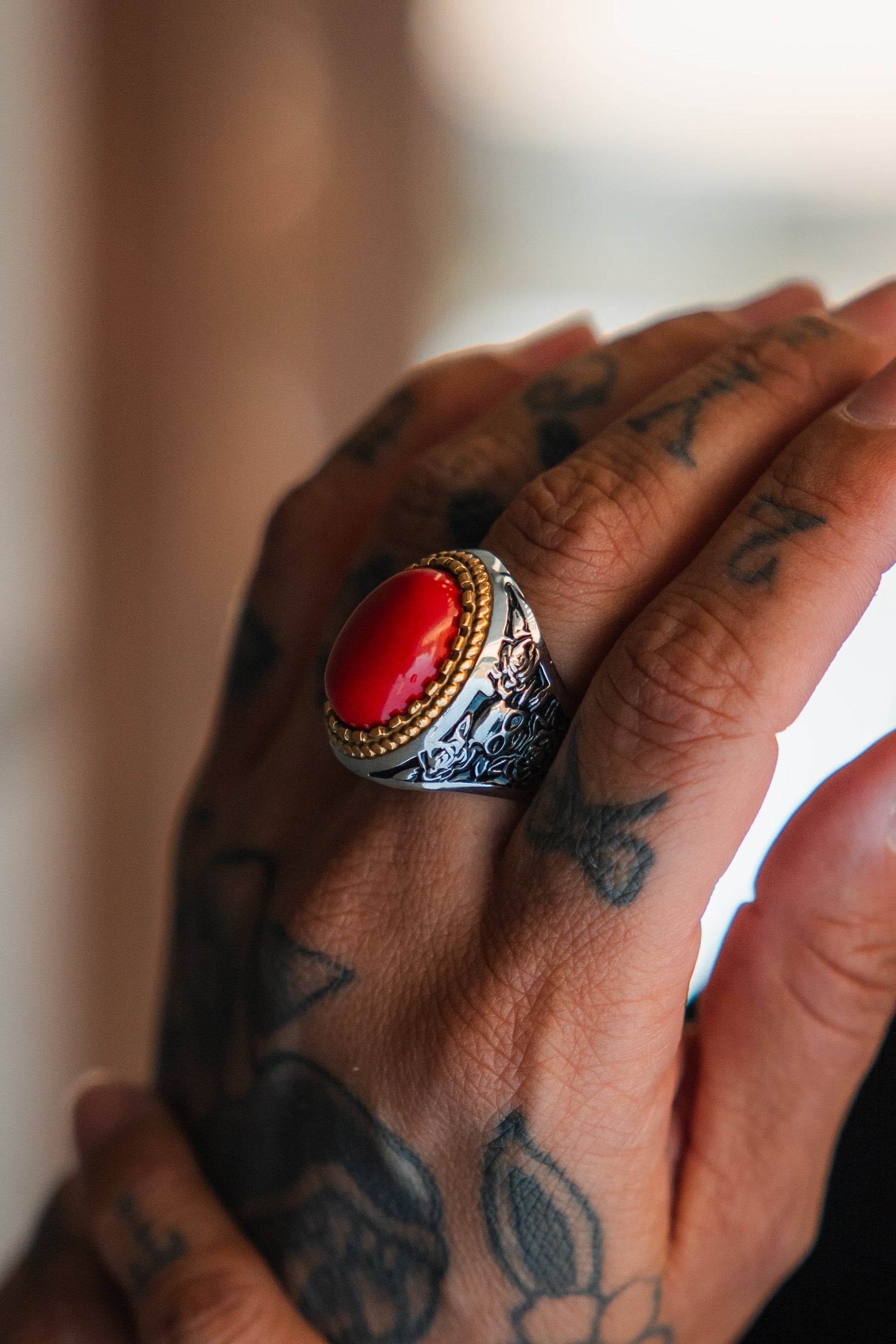 A tattooed hand wears the Relentless Betrayal Burning Rose Ring—handcrafted with a vivid red stone set in a silver band, gold accents, and detailed engraved designs.