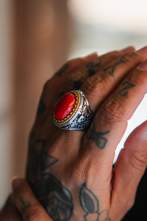 A tattooed hand wears the Relentless Betrayal Burning Rose Ring—handcrafted with a vivid red stone set in a silver band, gold accents, and detailed engraved designs.