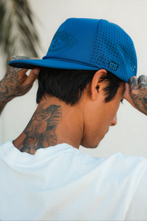 A person is seen from behind wearing a Relentless Betrayal Dark Waters SOS Mute PVC Snapback backwards and a white shirt, revealing neck and hand tattoos for a bold, adventurous look.