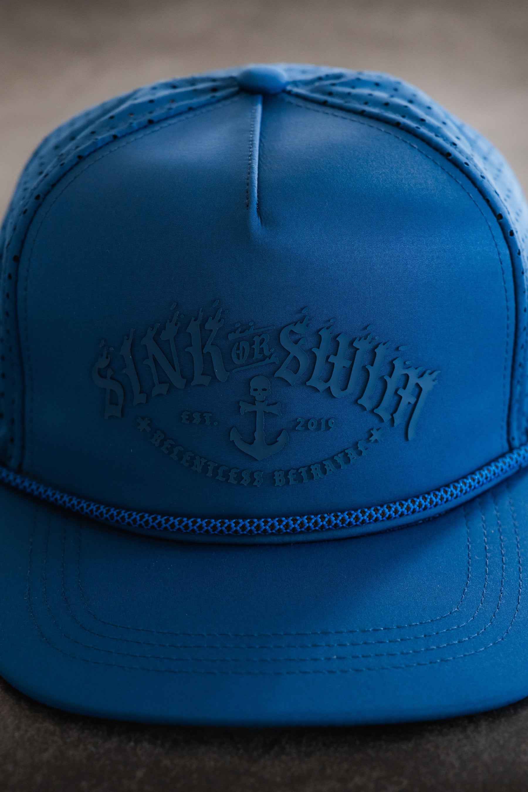 A close-up of the Dark Waters SOS Mute PVC Snapback by Relentless Betrayal, featuring a blue patch embossed with SINK OR SWIM, an anchor design, and small text reading EST. 2015 and RESCUERS BFF CLUB on the front.