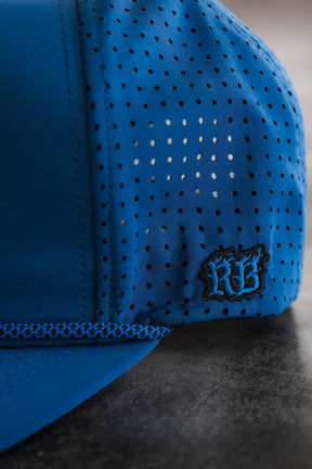 Close-up of the Relentless Betrayal Dark Waters SOS Mute PVC Snapback with small perforations, decorative stitching, and an embroidered black RF logo on the side, shown against a dark textured background. Water resistant, black finish.