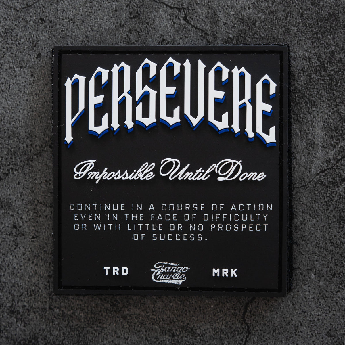 The Persevere - Patch by Tango Charlie Apparel features "PERSEVERE. Impossible Until Done" in white and blue on a textured gray background, resembling a classic 3D PVC or Velcro patch. Perfect for those who keep going against the odds.