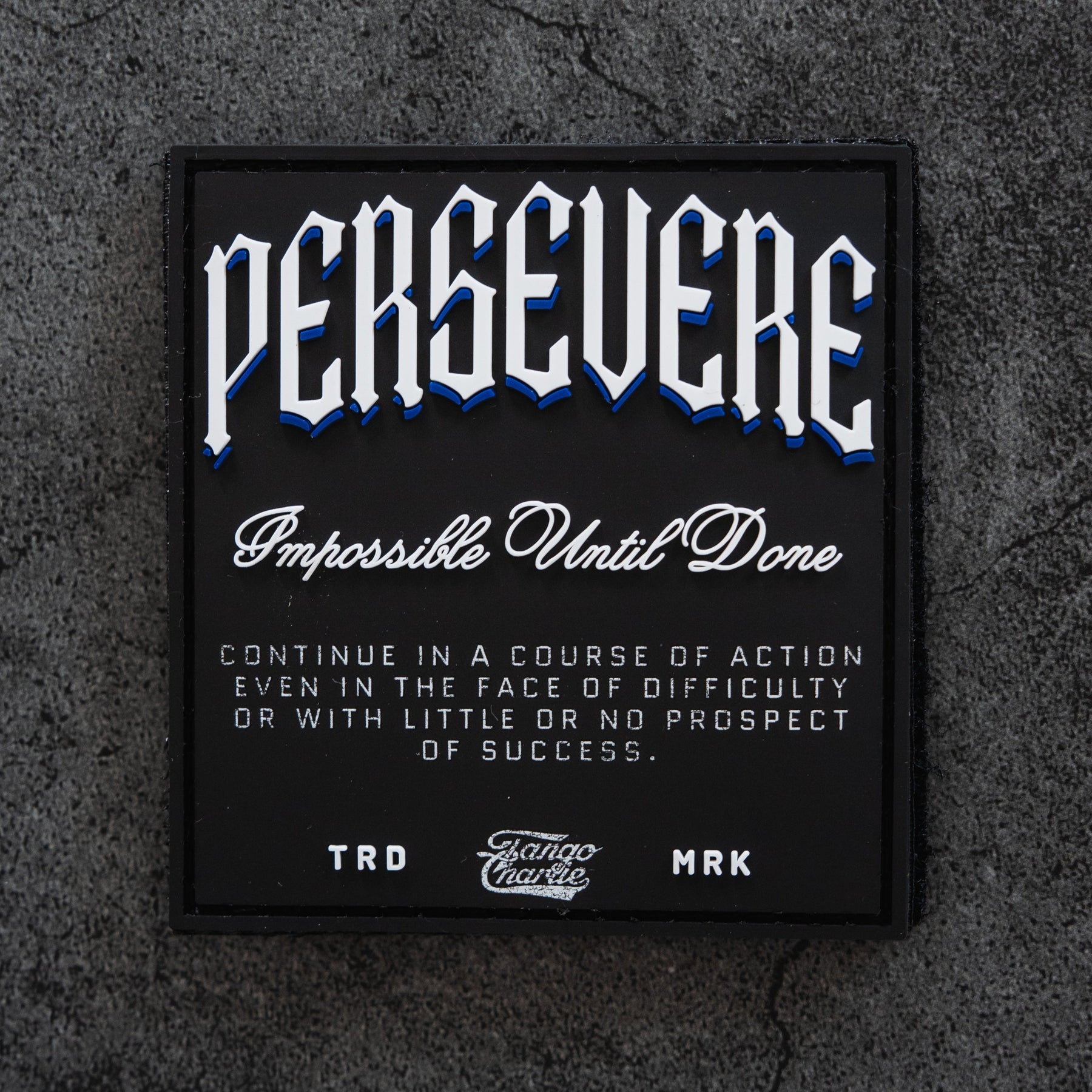 The Persevere - Patch by Tango Charlie Apparel features "PERSEVERE. Impossible Until Done" in white and blue on a textured gray background, resembling a classic 3D PVC or Velcro patch. Perfect for those who keep going against the odds.