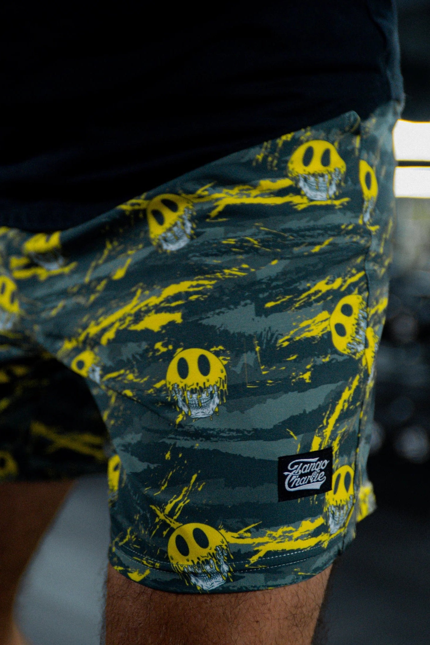 Close-up of Tango Charlie Apparel's Men's Performance Training Shorts | 5.5"- Savage, showcasing a yellow and gray camo print with melting smiley faces and a Fame Flame logo patch for bold style.