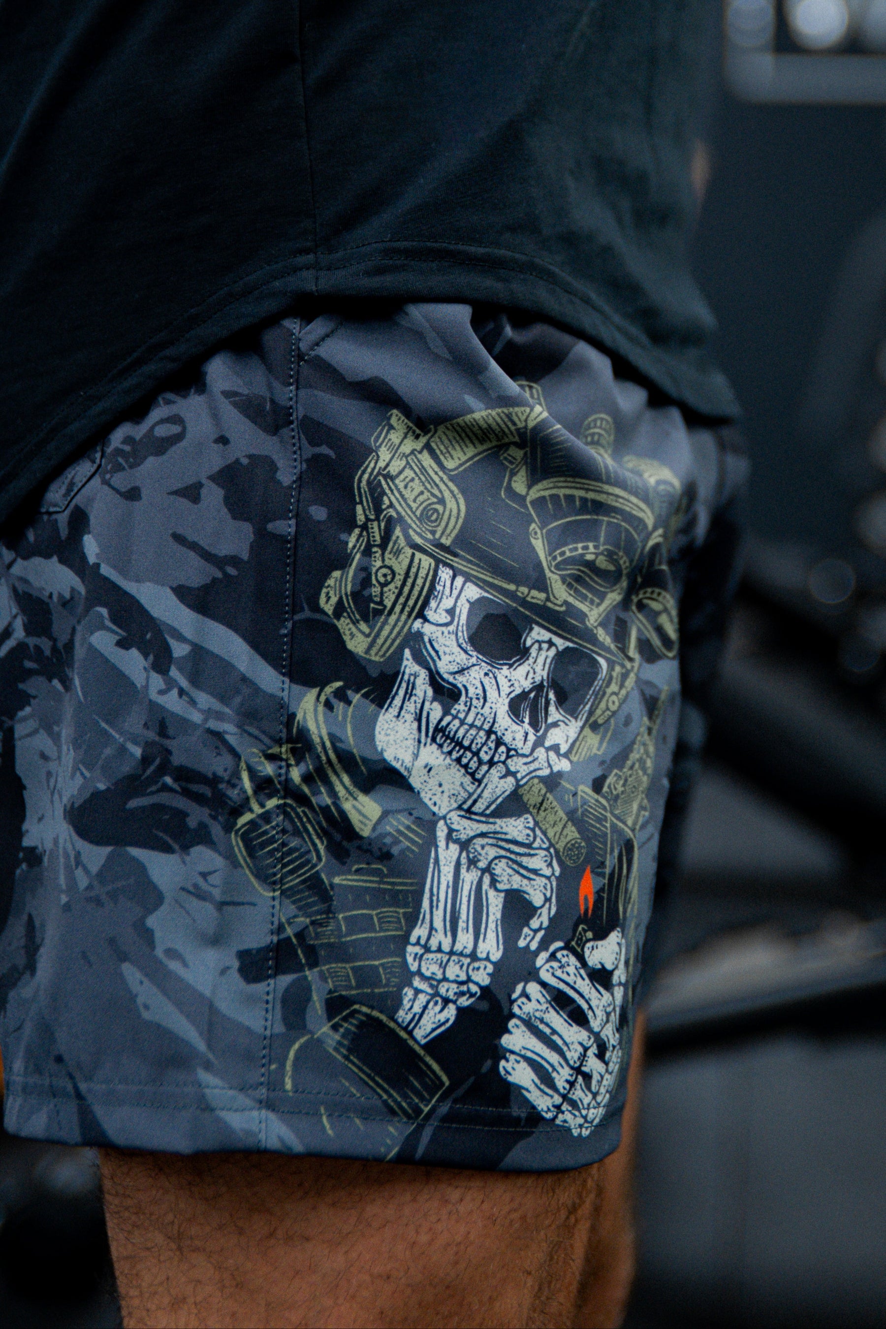 A close-up of a person wearing Born United Private Label Mens Performance Hybrid Shorts 5.5 | Savage Ops, which feature a detailed graphic of a skeleton soldier in a helmet lighting a cigarette with a visible red flame.
