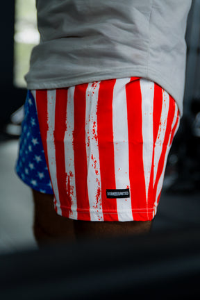 A person wears Born United Private Label Mens Performance Hybrid Shorts 5.5 | Stars & Stripes, featuring an American flag design and quick-drying athletic fabric.