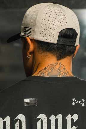 A person with short dark hair, shown from behind, wears the LHSG Hydro - Snapback Hat by Tango Charlie Apparel backwards, a black shirt with white graphic prints, and has an abstract flame tattoo on the back of their neck.