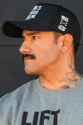 A man with a mustache and neck tattoos wears the Tango Charlie Apparel "No One Is Coming To Save You Hydro" snapback hat and a gray sweatshirt, looking to the side against a dark background.