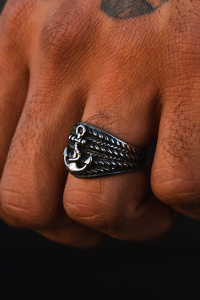 A close-up of a hand wearing The Gravewater Ring by Relentless Betrayal, featuring handcrafted silver with an anchor motif and rope details, showing skin texture and a partial knuckle tattoo.