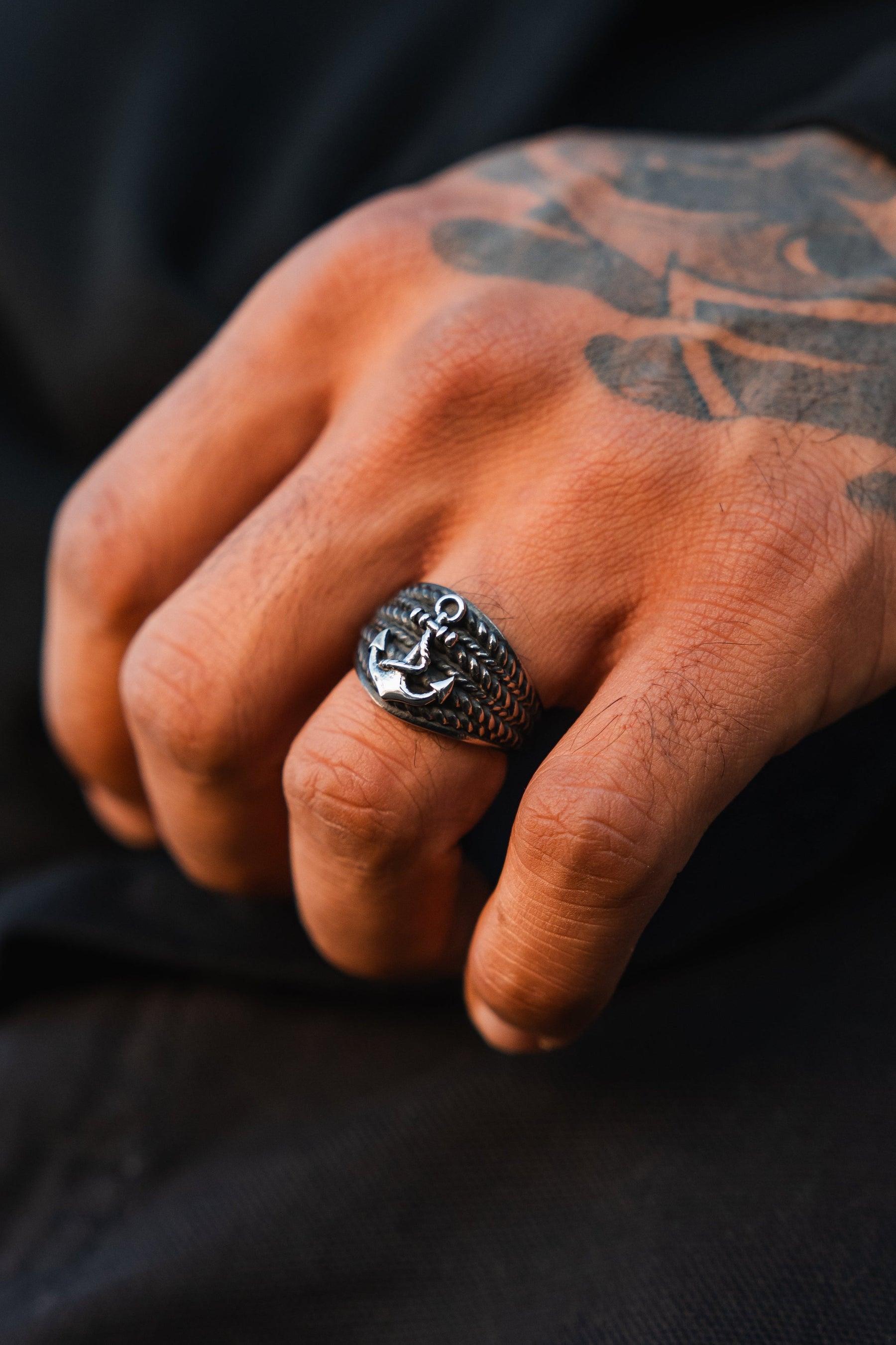 A tattooed hand wears The Gravewater Ring by Relentless Betrayal, a detailed stainless steel dragon’s head design, against a dark background.