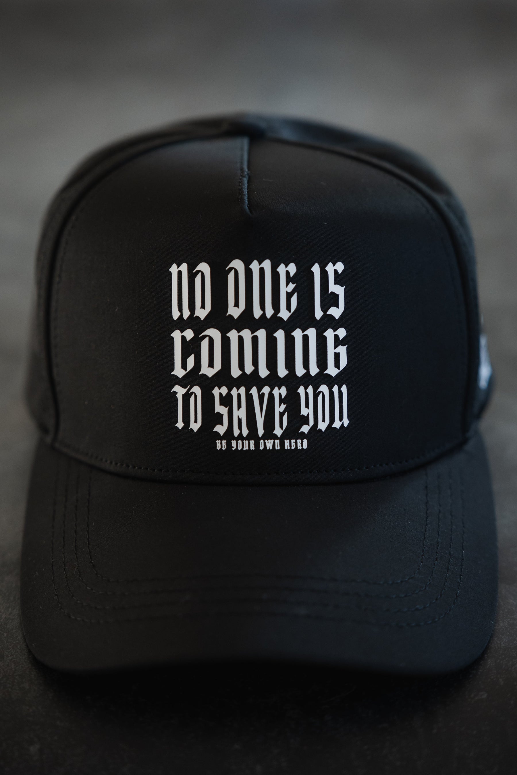 The Tango Charlie Apparel No One Is Coming To Save You Hydro Snapback Hat is black and breathable, featuring white gothic text—"No one is coming to save you. Be your own hero."—against a dark background.