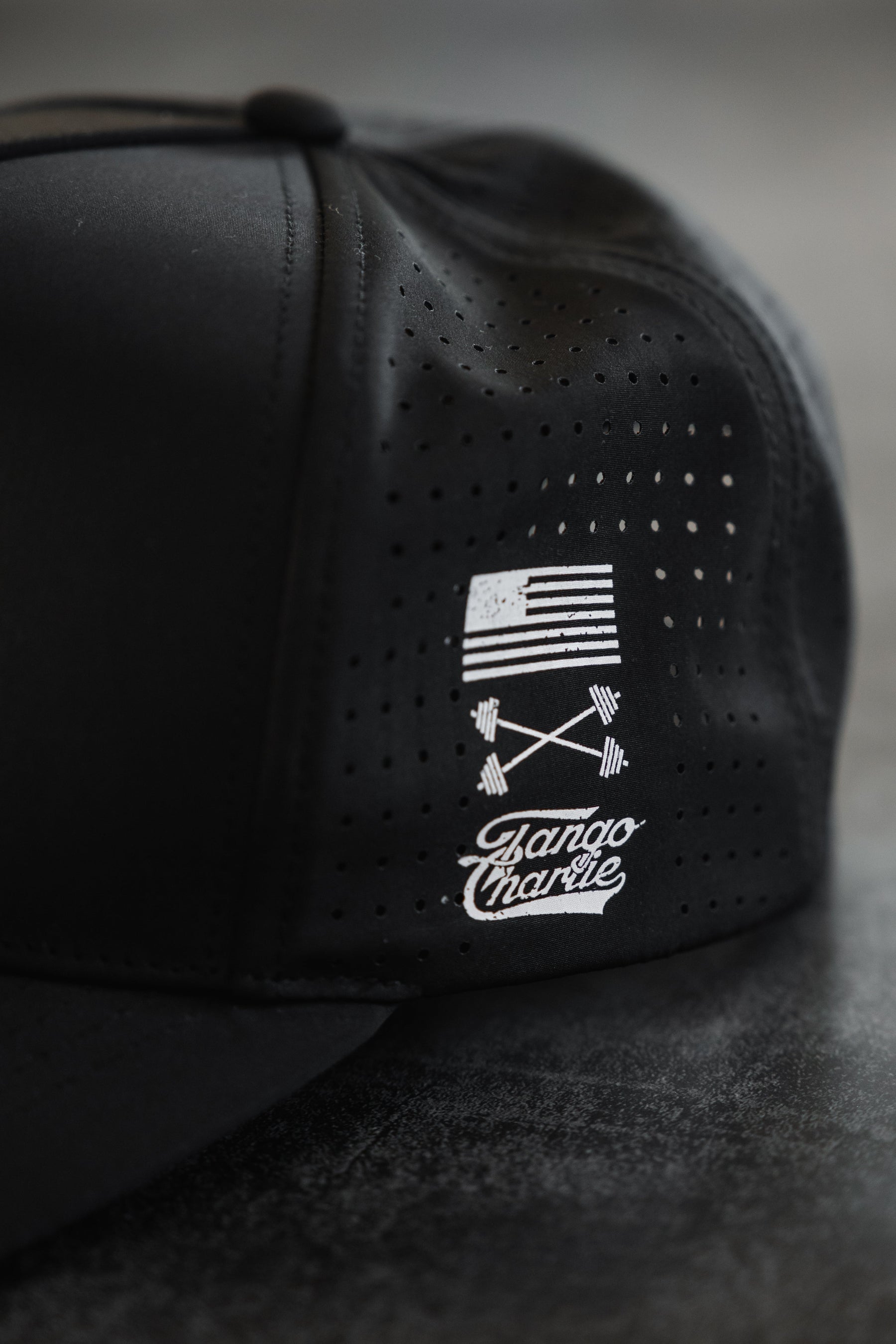The No One Is Coming To Save You Hydro - Snapback Hat by Tango Charlie Apparel is a black, breathable cap with tiny ventilation holes, featuring a small white American flag and crossed barbells graphic, plus Bando Charlie text on the side.