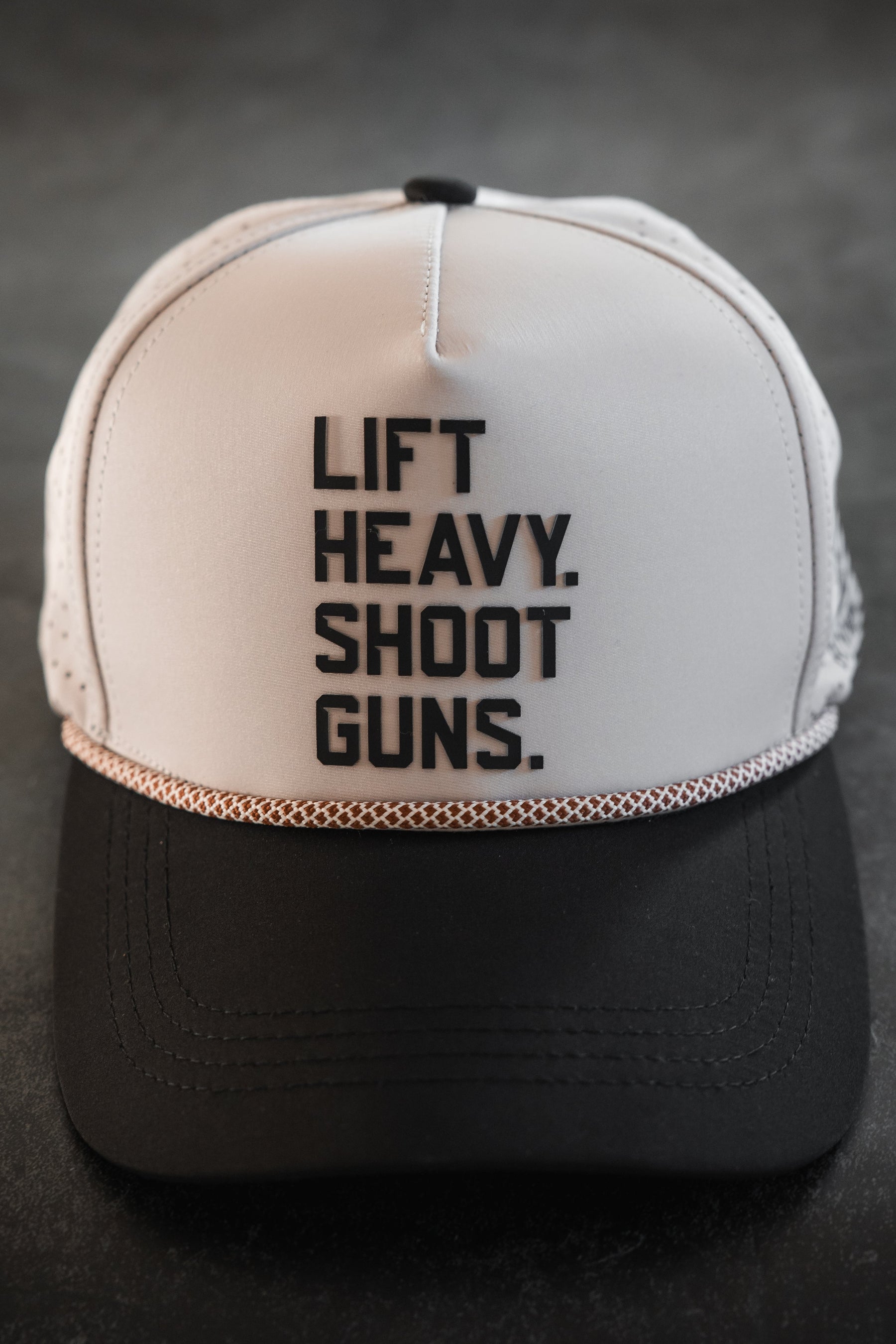 The LHSG Hydro - Snapback Hat by Tango Charlie Apparel features "LIFT HEAVY. SHOOT GUNS." in bold black letters on the front panel, shown here in a white and black design as part of their Born United collaboration.