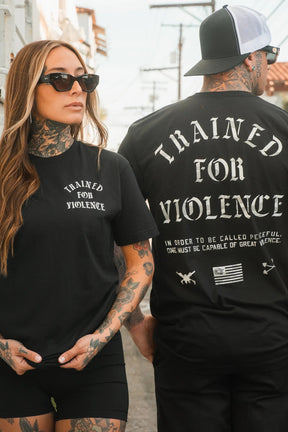 A tattooed man and woman wear Tango Charlie Apparel’s Trained for Violence Tee. Hers displays the bold slogan, while his shirt’s back states that true peace demands both strength and technical proficiency.