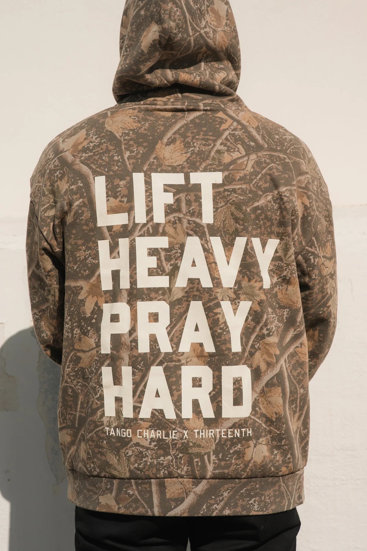 Person wearing the Lift Heavy. Pray Hard. - Deadwood Camo Hoodie by Tango Charlie Apparel, embodying resilience and spiritual strength in style.
