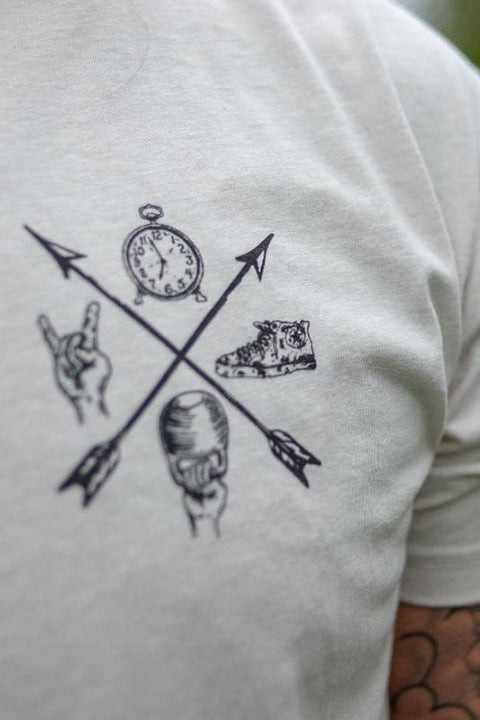 Close-up of the Doers Drifters Lifters Punks Unisex Tee by Tango Charlie Apparel, featuring two crossed arrows with a clock, sneaker, rock hand sign, and fist graphic. Tattooed arm partly visible—rep your crew in style.