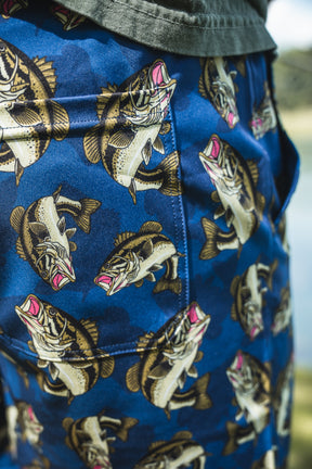 Close-up of Mucker Bucket Men's Performance Athletic Shorts | 5.5"- Big Bass Daddy, showing a bold fish pattern with pink details. Worn with a green shirt, these shorts offer playful style and everyday comfort.