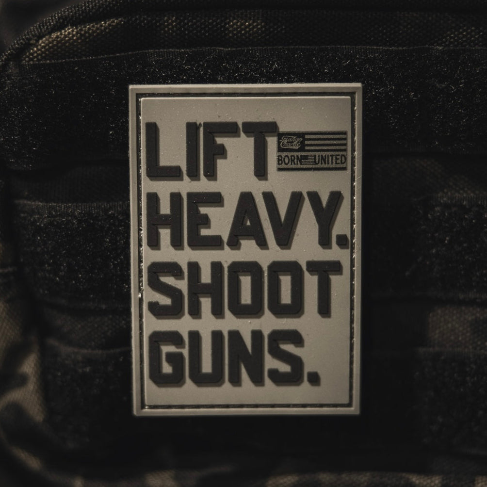The LHSG - Patch by Tango Charlie Apparel is a rectangular 3D PVC Velcro patch with bold black "LIFT HEAVY. SHOOT GUNS." text, a small American flag, and "BORN UNITED." in the top right corner.