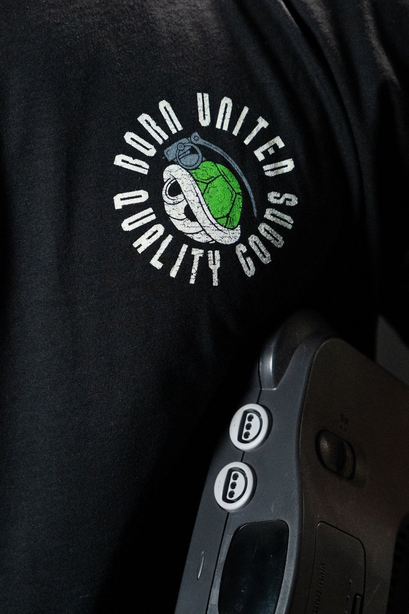 A man wearing a premium tee featuring a turtle graphic and the Born United Private Label logo holds a gray Super Merica Bros retro game console with two visible controller ports.