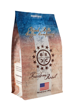 Black Rifle Coffee’s Freedom Roast Ground 12 oz features a rustic American flag design, brand logo, and a hint of milk chocolate flavor in every cup. A small American flag is displayed at the bottom of the packaging.
