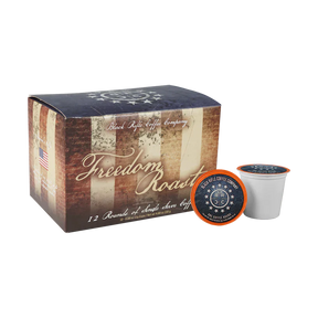 A box of Black Rifle Coffee Freedom Roast Rounds 12 Count features patriotic American flag graphics, with one single-serve pod in front highlighting milk chocolate and vanilla notes—celebrating America’s Coffee.
