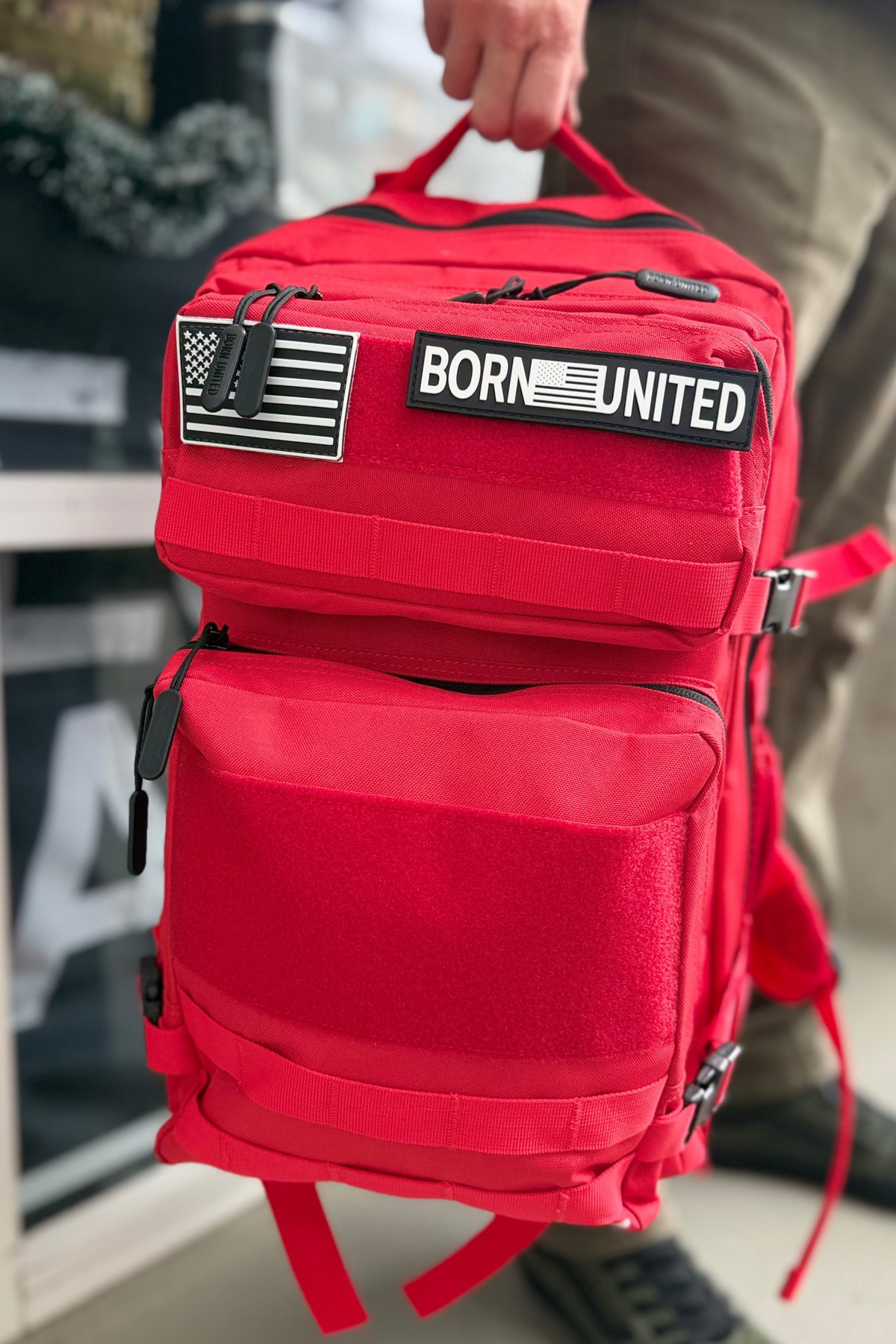 Red backpack with 'Born United' and American flag patch held by a person.