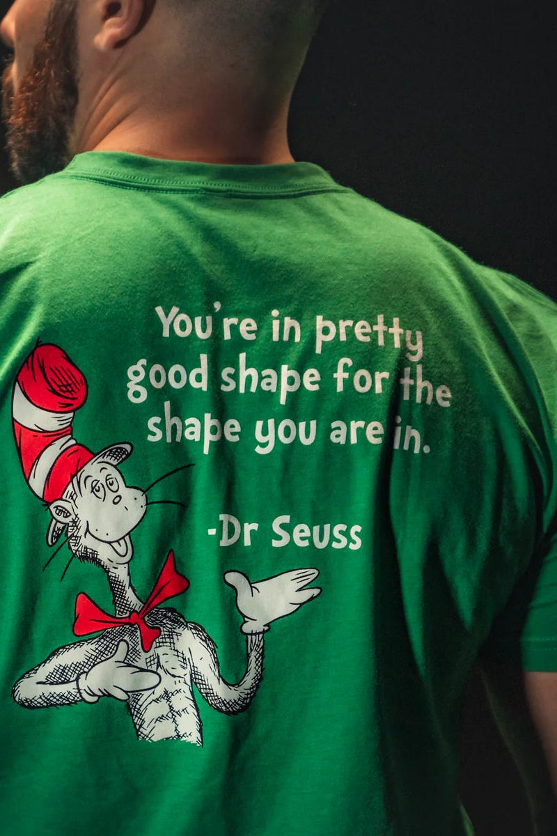 A man wears the St. Seuss Tee from Tango Charlie Apparel, featuring a green design with a Dr. Seuss character in a red hat and bow tie, along with the text: Youre in pretty good shape for the shape you are in, symbolizing resilience and self-improvement through whimsical wisdom.