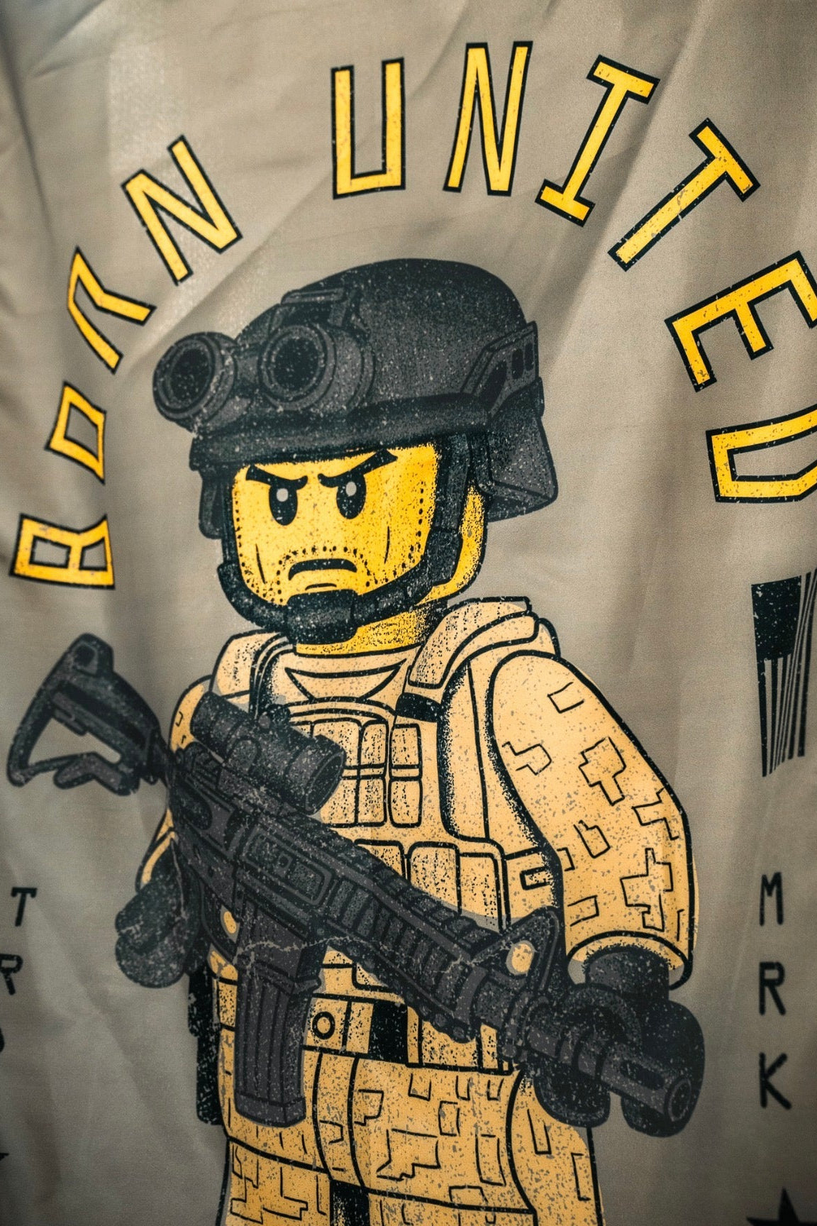 A LEGO-style soldier in desert camo with a rifle and helmet featuring night-vision goggles stands under the bold yellow "Born United" logo and the Brick Operator Flag by Born United Private Label.