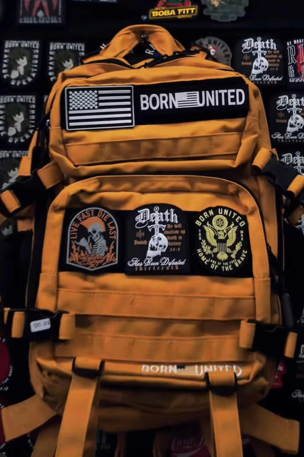 The Gold Glory Limited Ed. Tac-Pac - 45L by Born United Private Label is a yellow backpack with American flag, BORN UNITED, LIVE FAST DIE LAST, skull, and eagle patches, featuring luxury gold details that make its bold style shine.