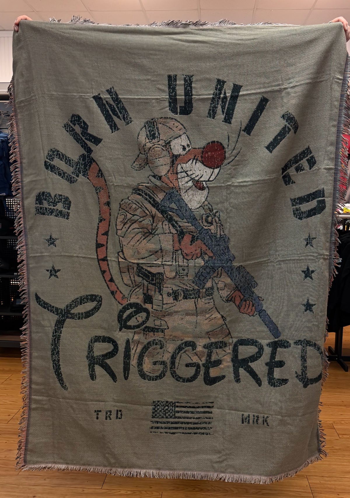 The Triggered Jacquard Blanket by Born United Private Label features a cartoon tiger in military gear with "Born United Triggered" text and a stylized American flag on an olive green background with fringed edges.