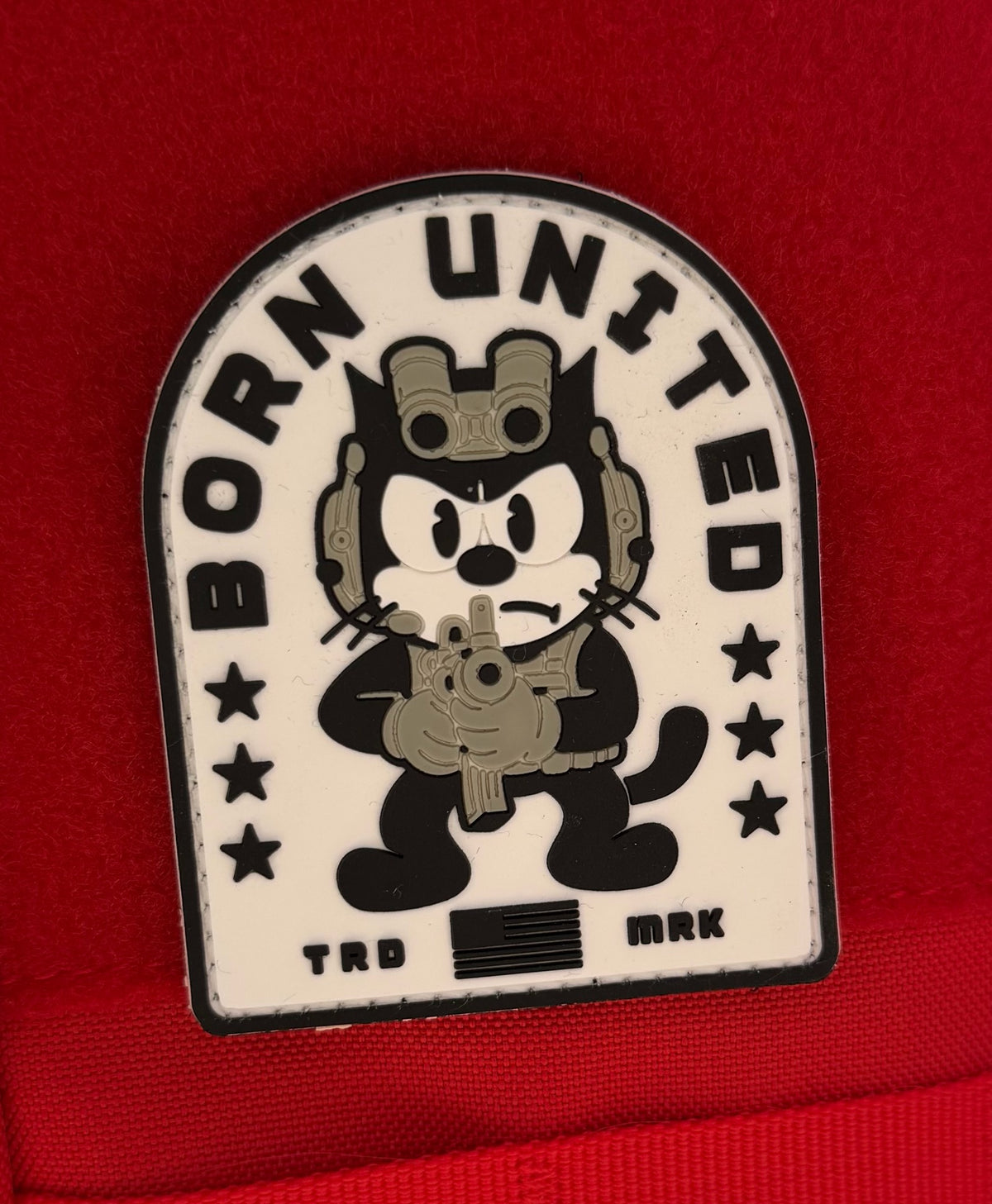 The Foxtrot Felix PVC Patch by Born United Private Label features a cartoon black cat in tactical gear holding a rifle, with “BORN UNITED” above, stars on each side, set against a red background.