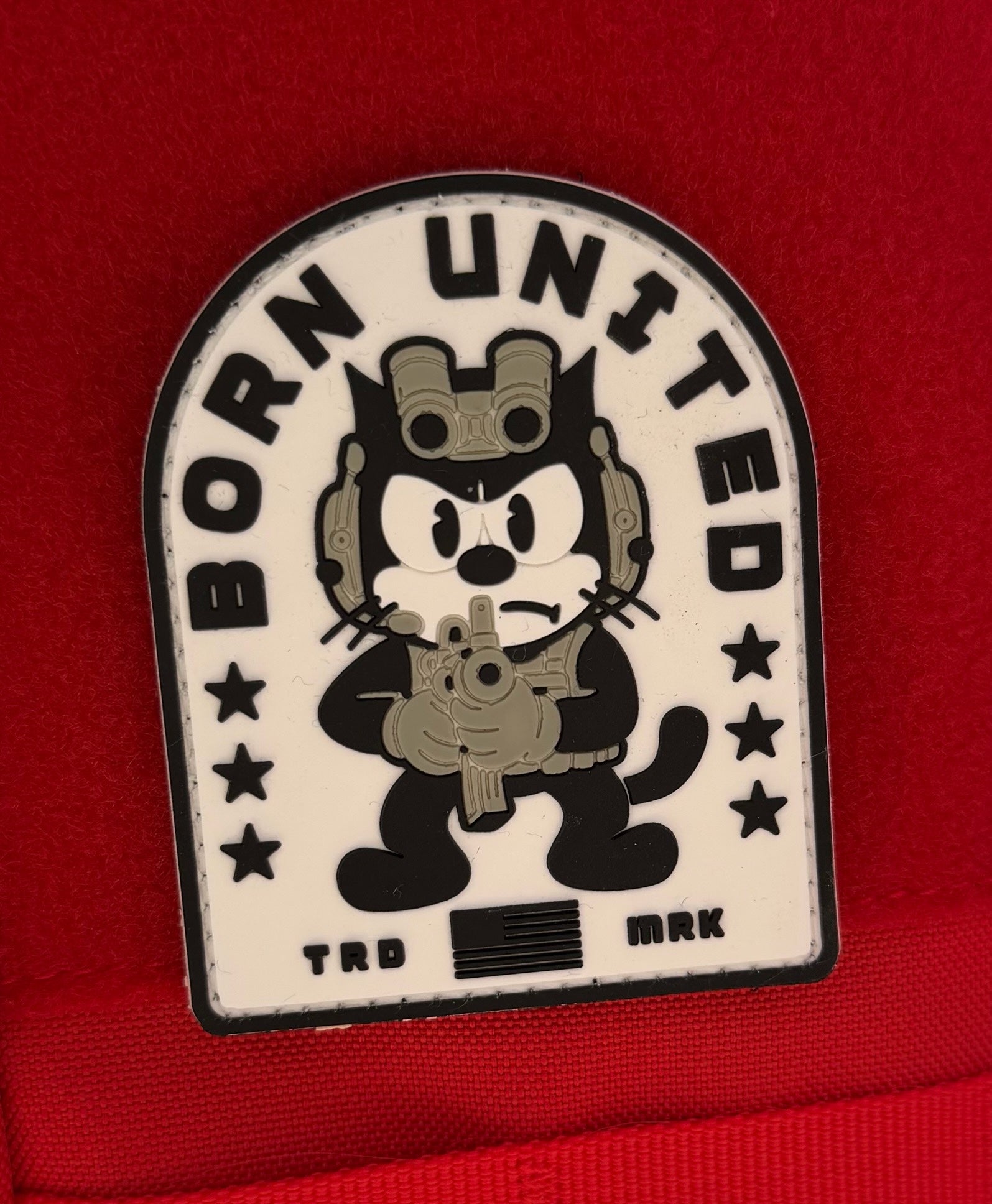 The Foxtrot Felix PVC Patch by Born United Private Label features a cartoon black cat in tactical gear holding a rifle, with “BORN UNITED” above, stars on each side, set against a red background.
